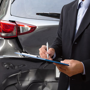 A man in a suit stands next to a car, writing on a clipboard. Relevant to 'Uninsured And Underinsured Motorist Claims In Maryland - The Yolles Legal Group