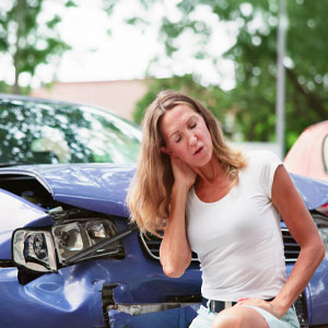 A woman sits on the side of a car, her head resting in her hands - The Yolles Legal Group